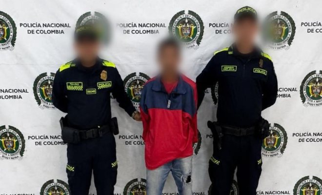 Dos funcionarios policiales con un ciudadano capturado frente a pendón institucional 