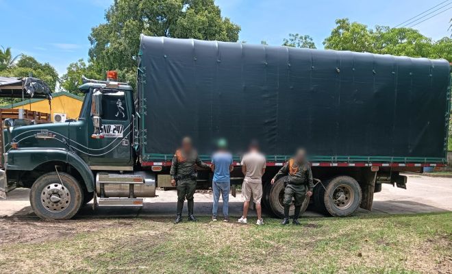dos uniformados de la policía nacional con dos personas  capturadas por por el presunto delito Policía Nacional captura a dos personas por aprovechamiento ilícito de los recursos naturales al frente se encuentra un camión color verde carrocería color negra  