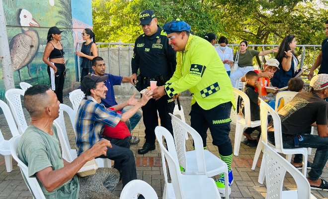 Dos funcionarios del grupo de policía comunitaria entregando alimentos a un grupo de personas habitantes de calle