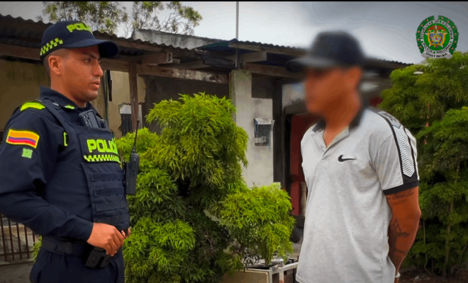 Un policía y una persona de camisa blanca permanecen de pie frente a frente; a su alrededor se observan árboles en un entorno al aire libre