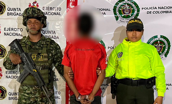 Persona capturada vestida con una camiseta color rojo siendo escoltado por funcionarios de la Policía Nacional y Ejercito de Colombia