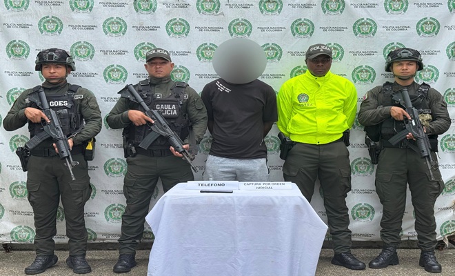 Uniformados de la Polic&iacute;a Nacional presentan a una persona capturada mediante orden judicial en Santa Rita de Ir&oacute;, Choc&oacute;. En el procedimiento participaron integrantes del GAULA y unidades policiales. Sobre una mesa se observa un tel&eacute;fono celular incautado como elemento material probatorio. Al fondo se aprecia un pend&oacute;n institucional de la Polic&iacute;a Nacional de Colombia.