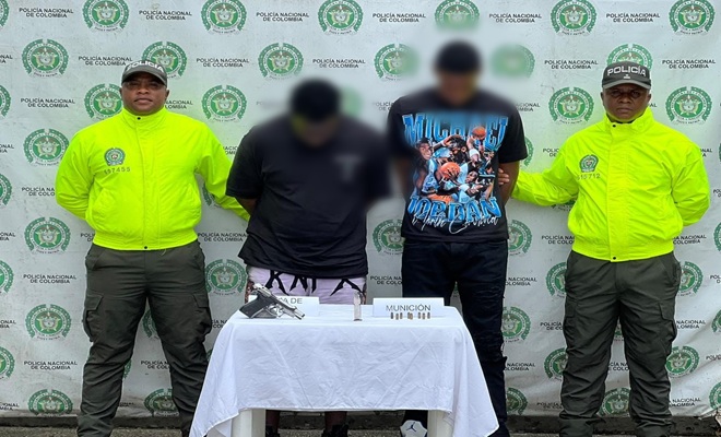 Uniformados de la Policía Nacional presentan a dos personas capturadas en Quibdó por el presunto delito de fabricación, tráfico, porte o tenencia de armas de fuego, accesorios, partes o municiones. En la mesa de evidencia se observa un arma de fuego, munición y elementos incautados durante el procedimiento