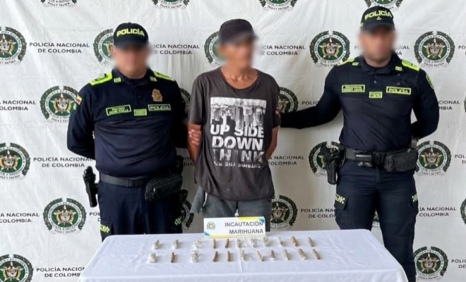 Dos funcionarios policiales con un ciudadano capturado frente a pendón institucional, delante una mesa con el material incautado
