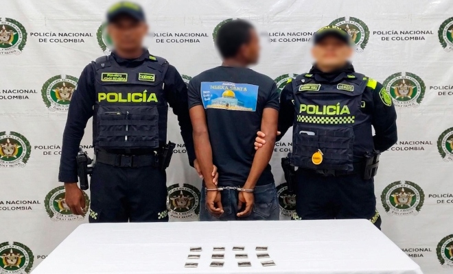 Dos funcionarios policiales junto a un ciudadano capturado frente a pendón institucional frente a ellos una mesa sobre la cual esta material incautado