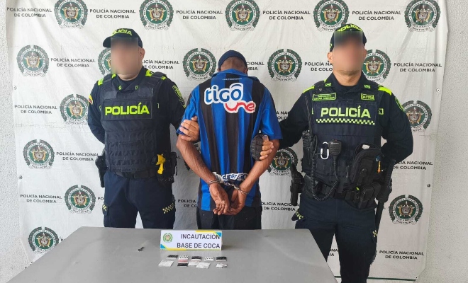 Dos funcionarios policiales junto a un ciudadano capturado frente a pendón institucional frente a ellos una mesa sobre la cual están las sustancias estupefacientes incautadas 