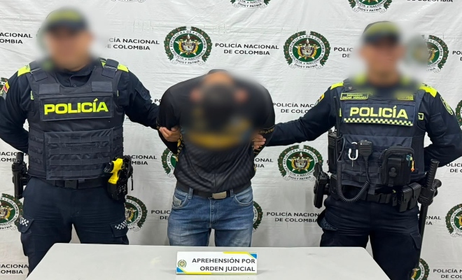 Dos funcionarios policiales con un ciudadano capturado por orden judicial frente al pend&oacute;n institucional