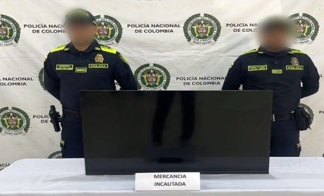 dos policias y en la mesa un televisor incautado 