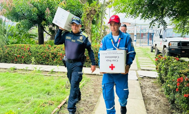 un  uniformado con un funcionario de la cruz roja trasladando cajas de ayuda 