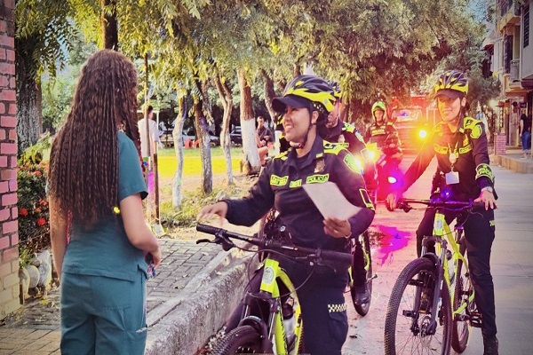 Tres Polic&iacute;as de patrulla purpura en campa&ntilde;as preventivas, una Polic&iacute;a entregando volante a una ciudadana 