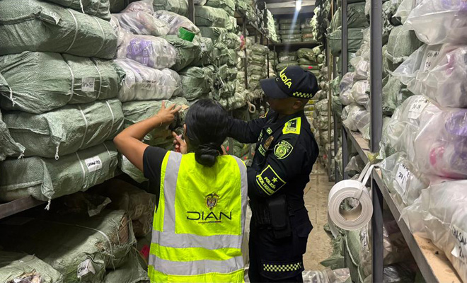 Un policía de la policía fiscal y aduanera y un funcionario de la dian inspeccionan mercancía ilegal hallada en varios paquetes
