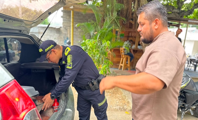 un uniformado de la Policía nacional  realizando un registro y control a un vehículo en vía principal en la parte trasera se encuentra un ciudadano  
