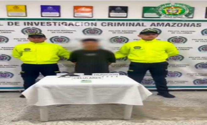 dos uniformados con chaqueta verde clara y un capturado en el centro con el fondo de un cartel blanco con logos de la policía nacional 