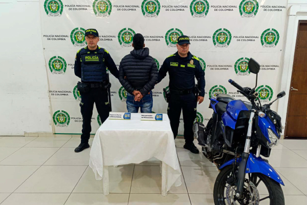 Hombre capturado de espalda en medio de dos Policías, en frente se encuentra la motocicleta recuperada