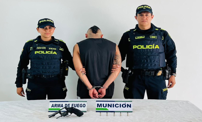 Hombre capturado en medio de dos Policías, en frente arma incautada