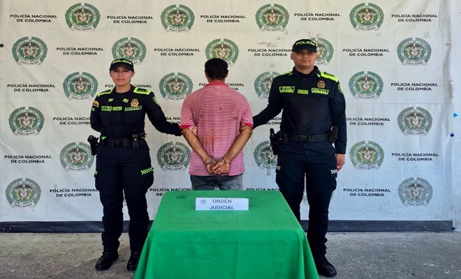 Un hombre de espaldas capturado por orden judicial por el delito de hurto y dos Policías brindando seguridad.