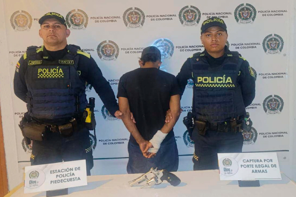 Hombre capturado en medio de dos policías, en frente arma incautada
