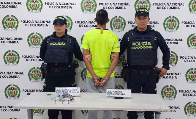 Hombre capturado en medio de dos Policías y un arma de fuego encima de una mesa