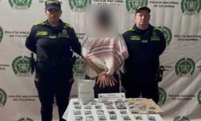 Hombre capturado en medio de dos policías, en frente mesa con estupefacientes incautados