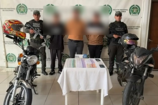 Hombres capturados en medio de dos policías, en frente dinero recuperado y a los lados motocicletas inmovilizadas