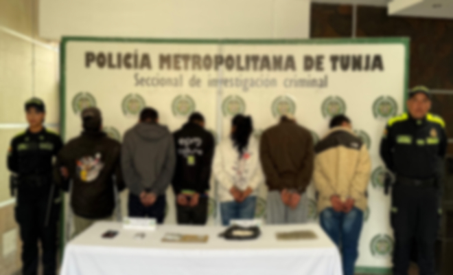 dos policías a los lados y en la mitad 6 personas capturadas con una mesa y elementos incautados