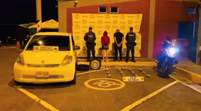 Dos polic&iacute;as al lado de dos personas capturadas con estupefacientes