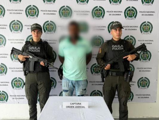 dos polic&iacute;as al lado de un hombre capturado por orden judicial