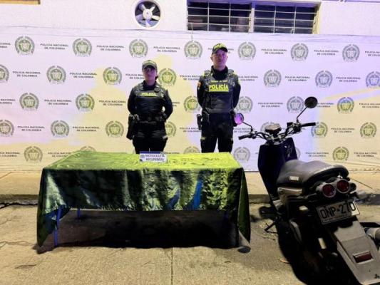 Dos policías al lado de una mesa una motocicleta recuperada