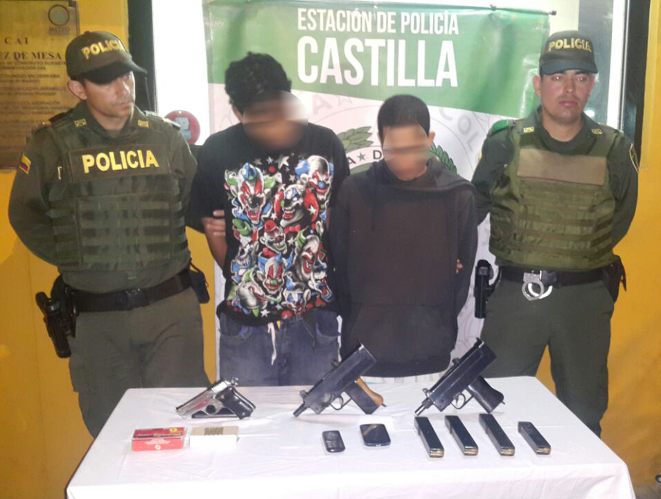 Dos policías custodian dos hombres capturados con armas en Medellín