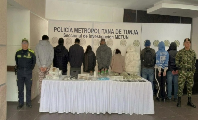 se encuentran 10 personas de espaldas, un funcionario de la policía al lado izquierdo y un funcionario del ejercito al lado derecho con una mesa y elementos incautados