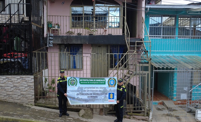 Dos uniformados con un cartel de extinción de dominio