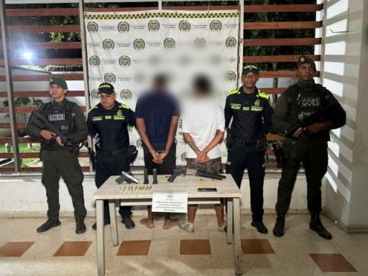 cuatro policías al lado de dos hombres capturados con armas de fuego