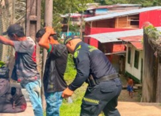 un uniformado realizando registro a dos hombre los cuales tienen las manos en la nuca