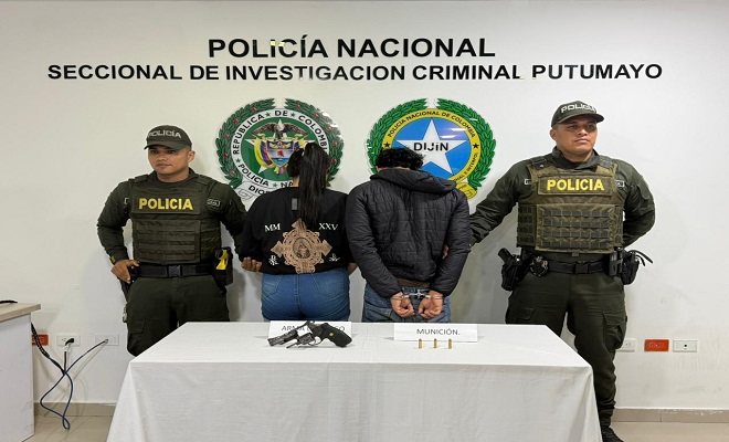 Dos polic&iacute;as y en medio un hombre y una mujer capturados frente a una mesa donde hay un rev&oacute;lver incautado en operativo policial 